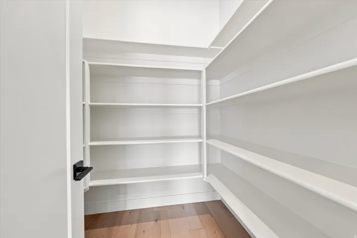 Expansive pantry featuring ample white shelving, wood-finish flooring, and a modern matte black door handle