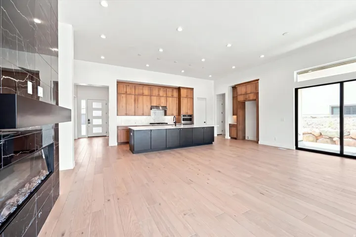 Open-concept living space with light wood-finish flooring, a contemporary fireplace with dark stone tiling, and a kitchen featuring dark base cabinetry and lighter wood-tone upper cabinetry