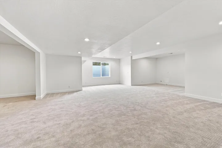 Spacious room with plush carpeting, recessed lighting, and a window with horizontal blinds