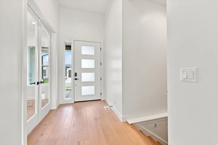 Entryway featuring wood-finish flooring, a contemporary door with frosted glass panels, an adjacent sidelight, and double glass-paneled doors