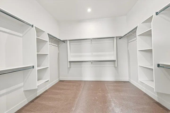Expansive walk-in closet featuring white built-in shelving, multiple hanging rods, and recessed lighting