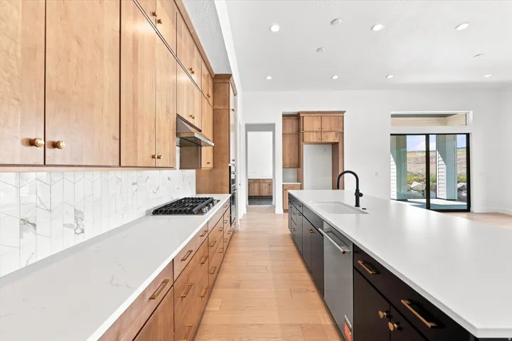 Light wood-finish cabinetry with brass hardware, white countertops, gas cooktop, and chevron tile backsplash