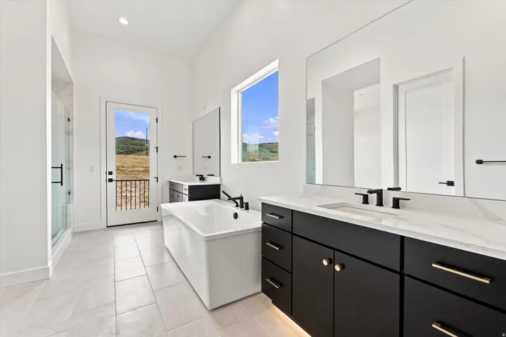 Bright bathroom featuring a freestanding tub, glass-enclosed shower, dual vanity with undermount sinks, and a large window