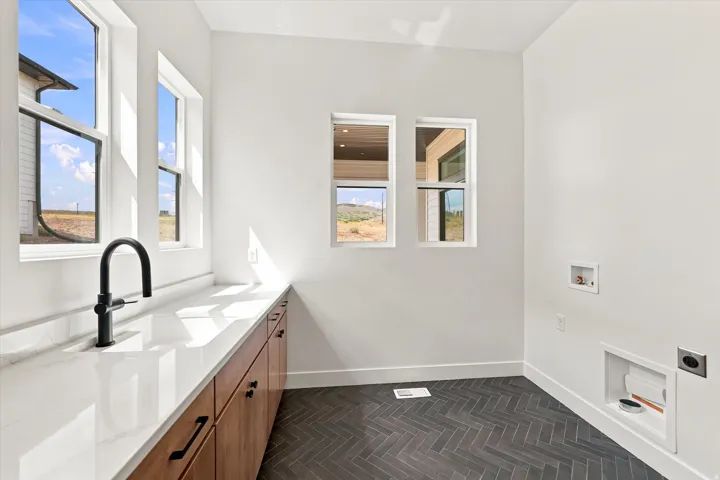 White countertop with an undermount sink and matte black faucet, wood-finish cabinetry with black hardware, and dark herringbone-patterned flooring