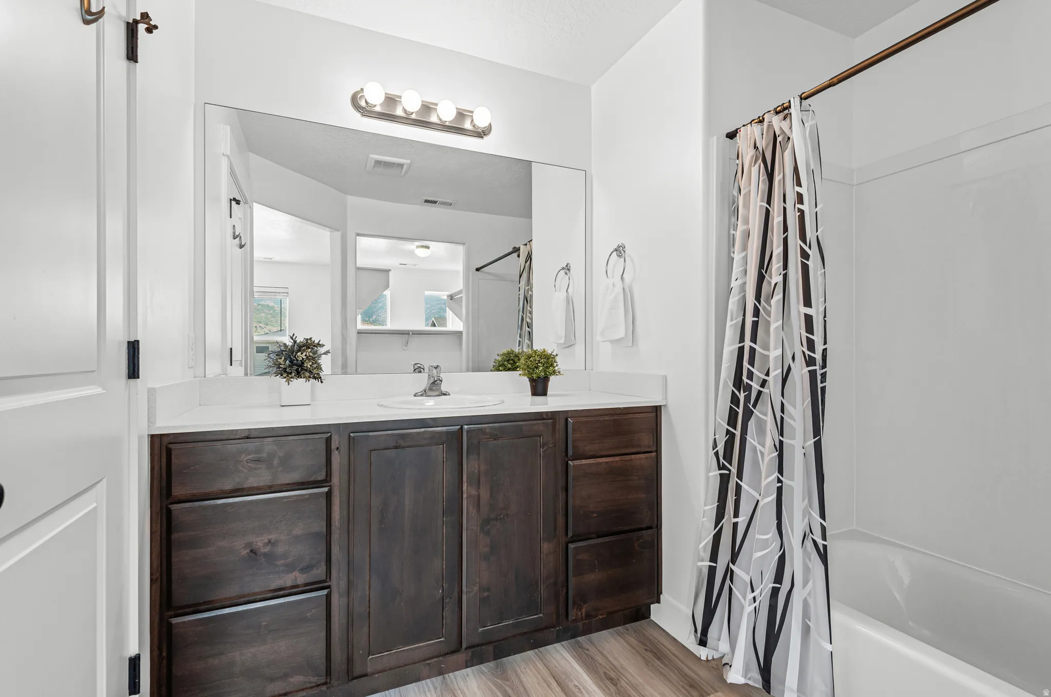 Bathroom featuring a wood-finish vanity with a white countertop and integrated sink, brushed nickel faucet, and a large mirror