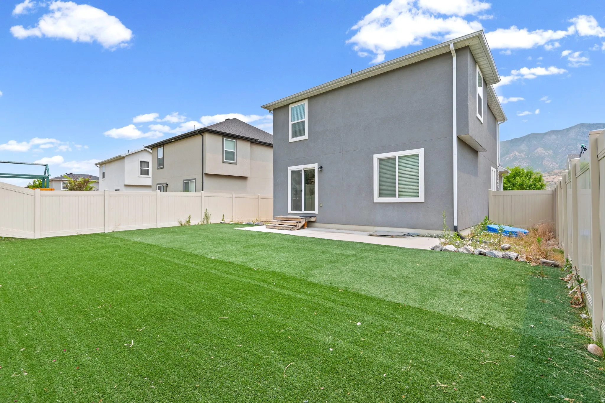 Expansive backyard featuring artificial turf, a privacy fence, and a concrete patio