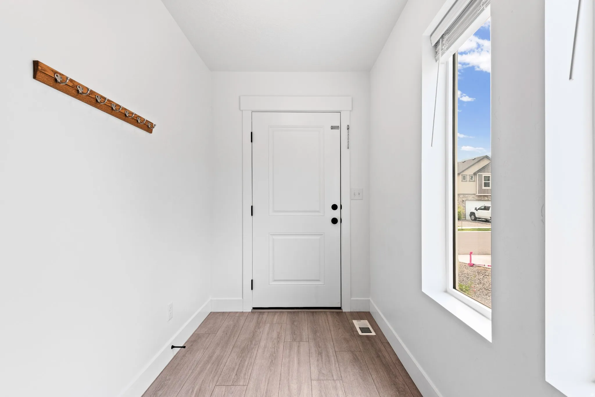 Entryway featuring wood-finish flooring, a white paneled door, and a tall window with privacy blinds