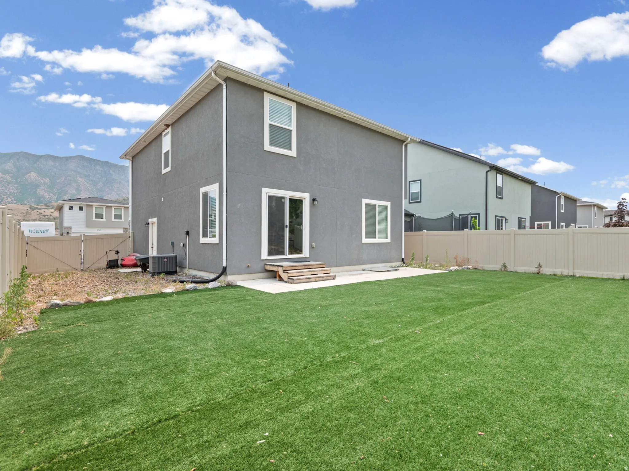 Expansive artificial turf backyard featuring a concrete patio pad and a full privacy fence