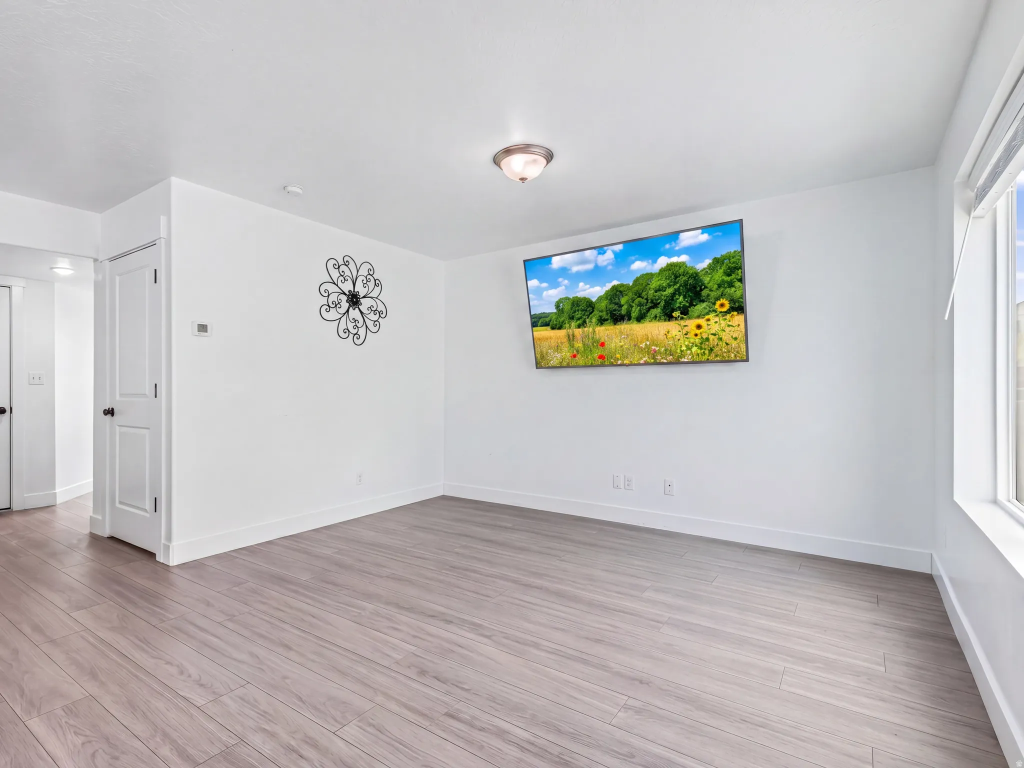 Bright living area featuring wood-finish flooring, white walls, white baseboards, and a large window providing ample natural light