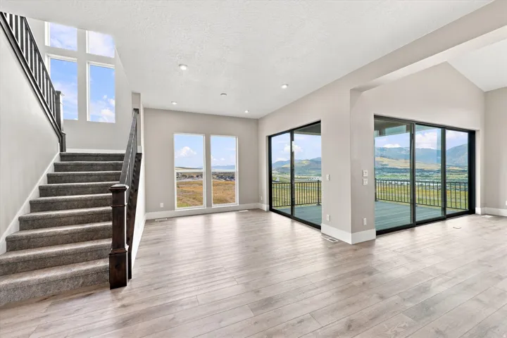 Expansive living area with wood-finish flooring, recessed lighting, and a staircase featuring carpeted treads and dark wood newel posts