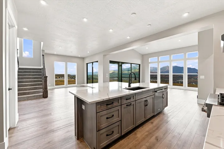 Expansive room with wood-finish flooring, a kitchen island featuring a sink and dishwasher, recessed lighting, and large windows