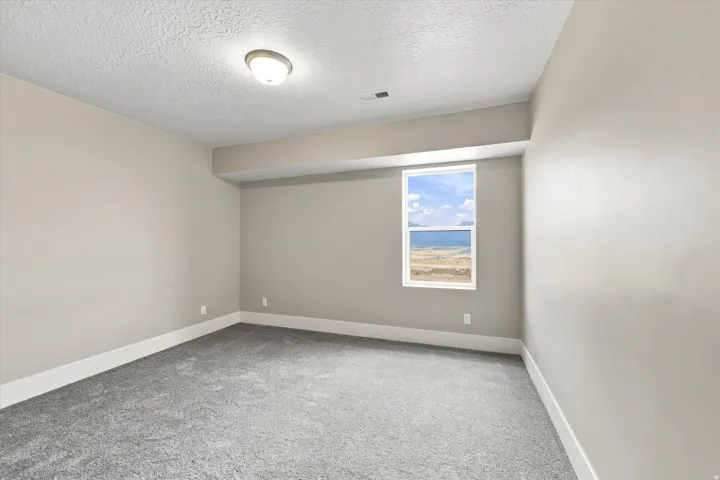 Neutral wall paint, gray carpet flooring, white trim, recessed ceiling light, and window with expansive water scenery