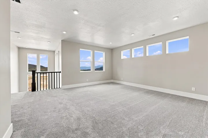 Spacious carpeted room featuring recessed lighting, multiple windows, a black spindle railing, and a neutral color palette