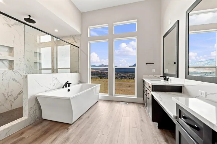 Freestanding soaking tub, walk-in shower with glass enclosure, dual vanity with undermount sinks, and wood-finish flooring