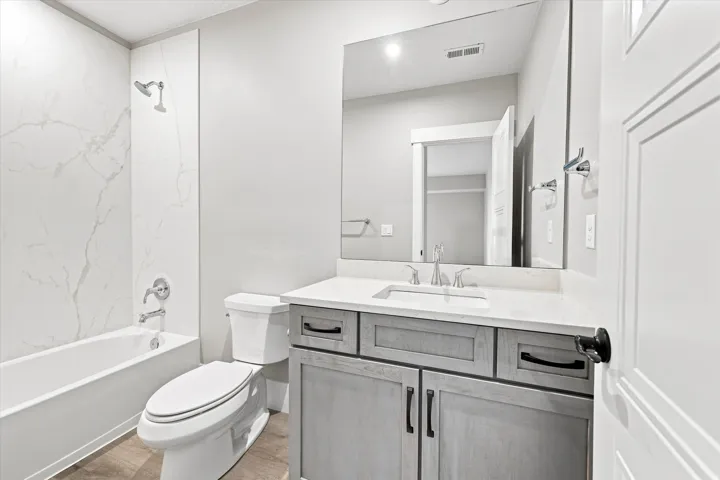 Bathtub with a shower head, toilet, vanity with a rectangular sink, wall-mounted mirror, and wood-finish flooring