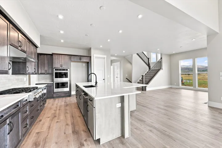 Modern kitchen featuring wood-finish flooring, dark wood cabinetry, white countertops, and stainless steel appliances
