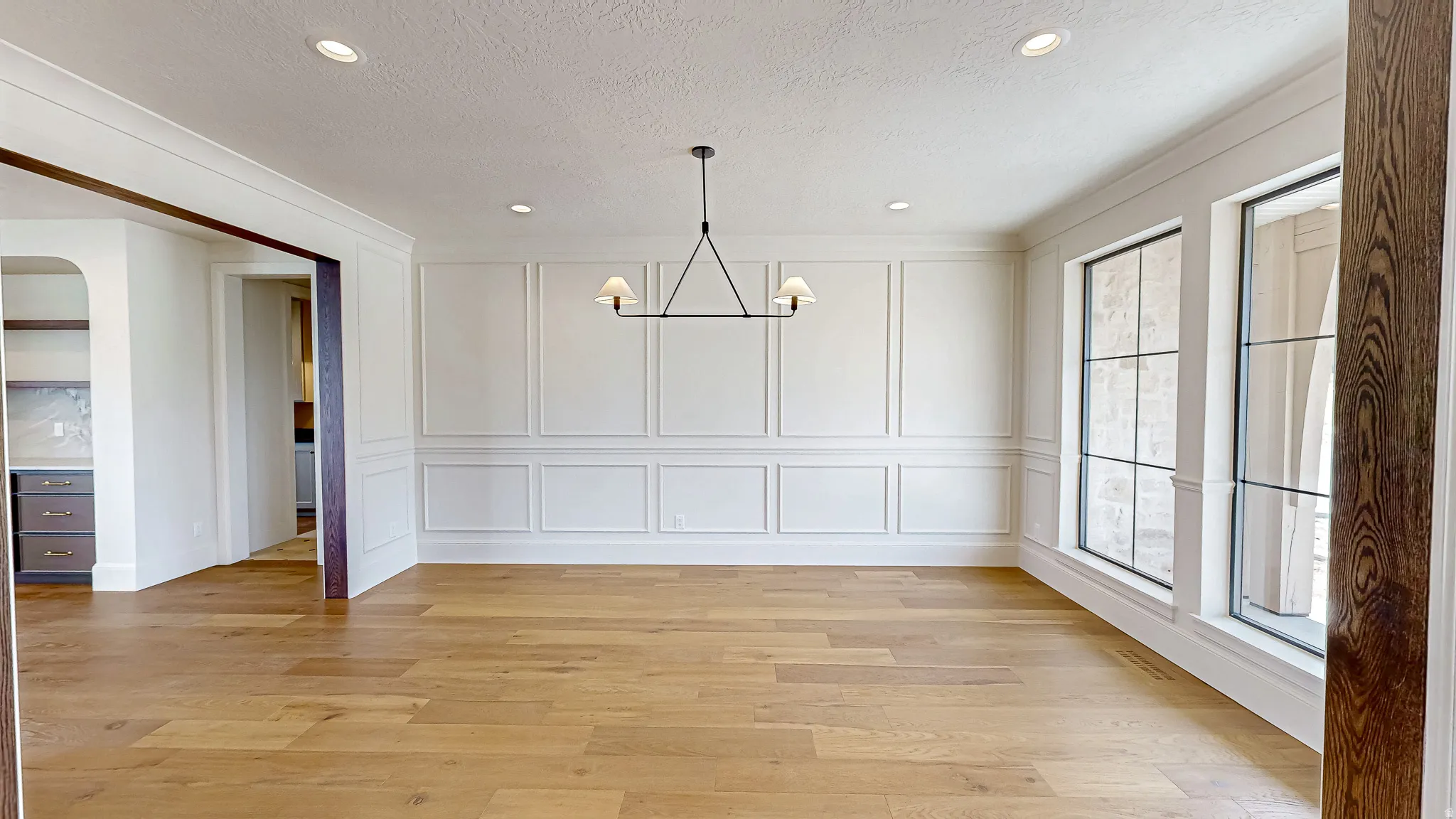 Spacious room featuring wood-finish flooring, wainscoting, recessed lighting, and a linear chandelier