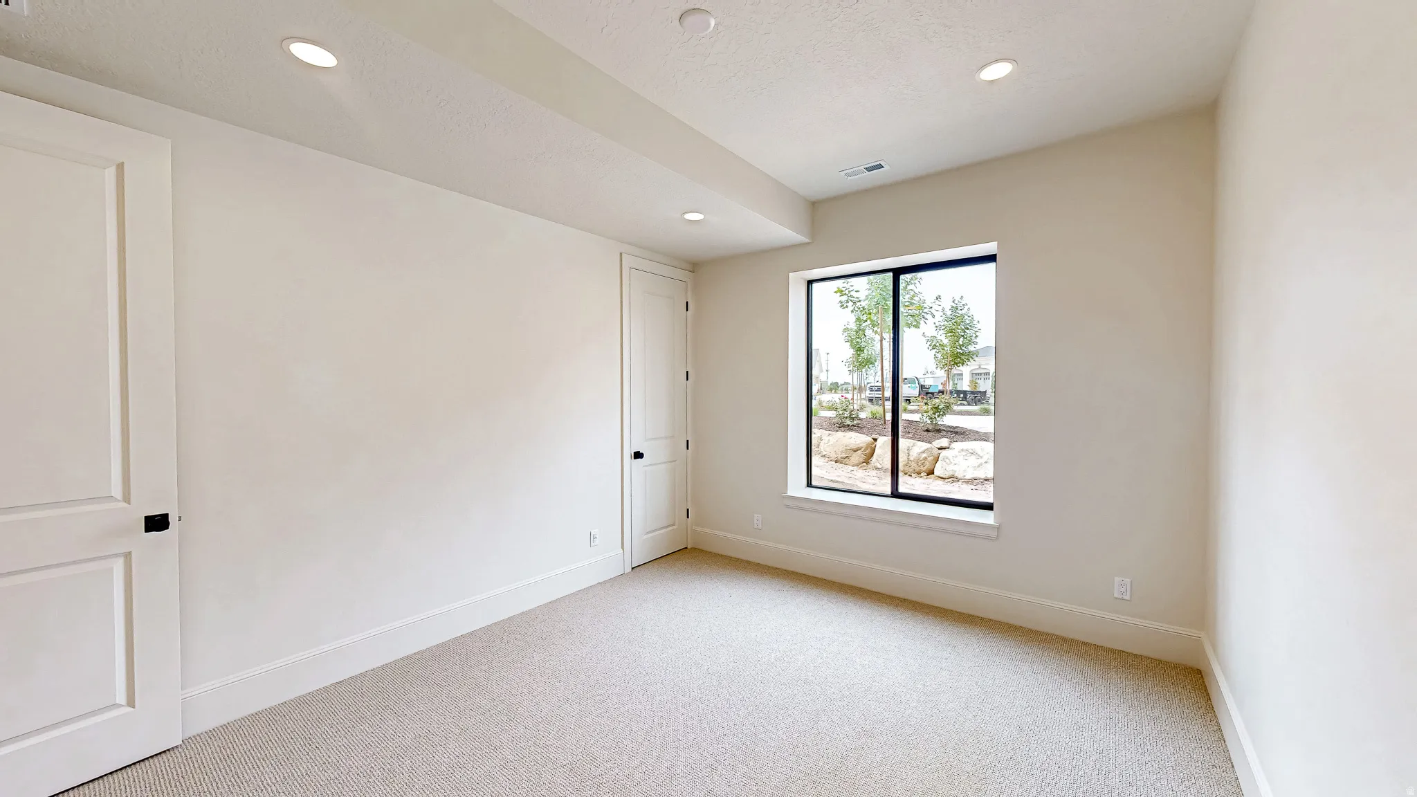 Carpeted room featuring recessed lighting, a large picture window with black trim, and two paneled doors with black hardware