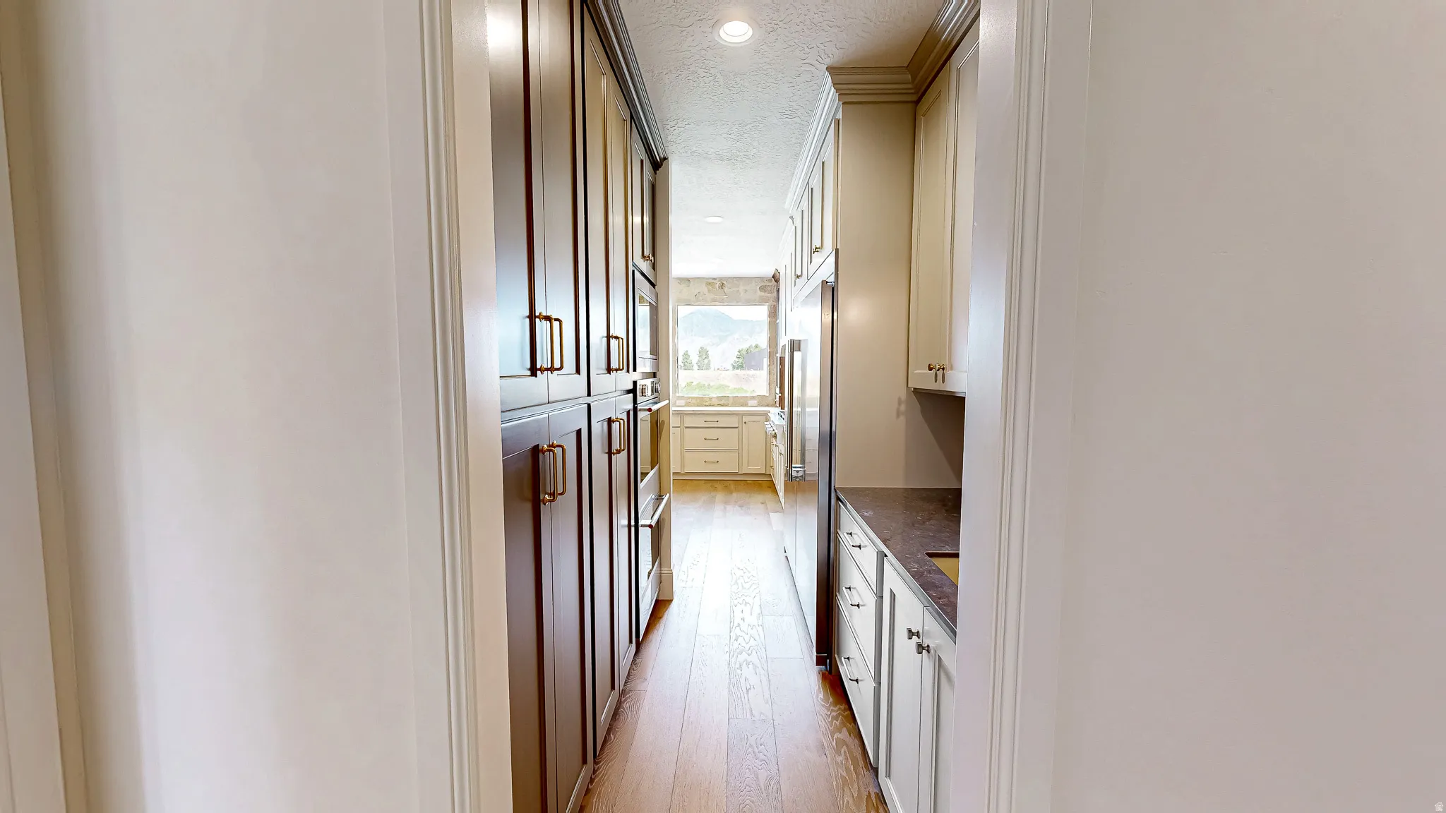 Galley kitchen featuring extensive dark wood cabinetry with bronze hardware, light wood-finish flooring, recessed lighting, and a stainless steel refrigerator