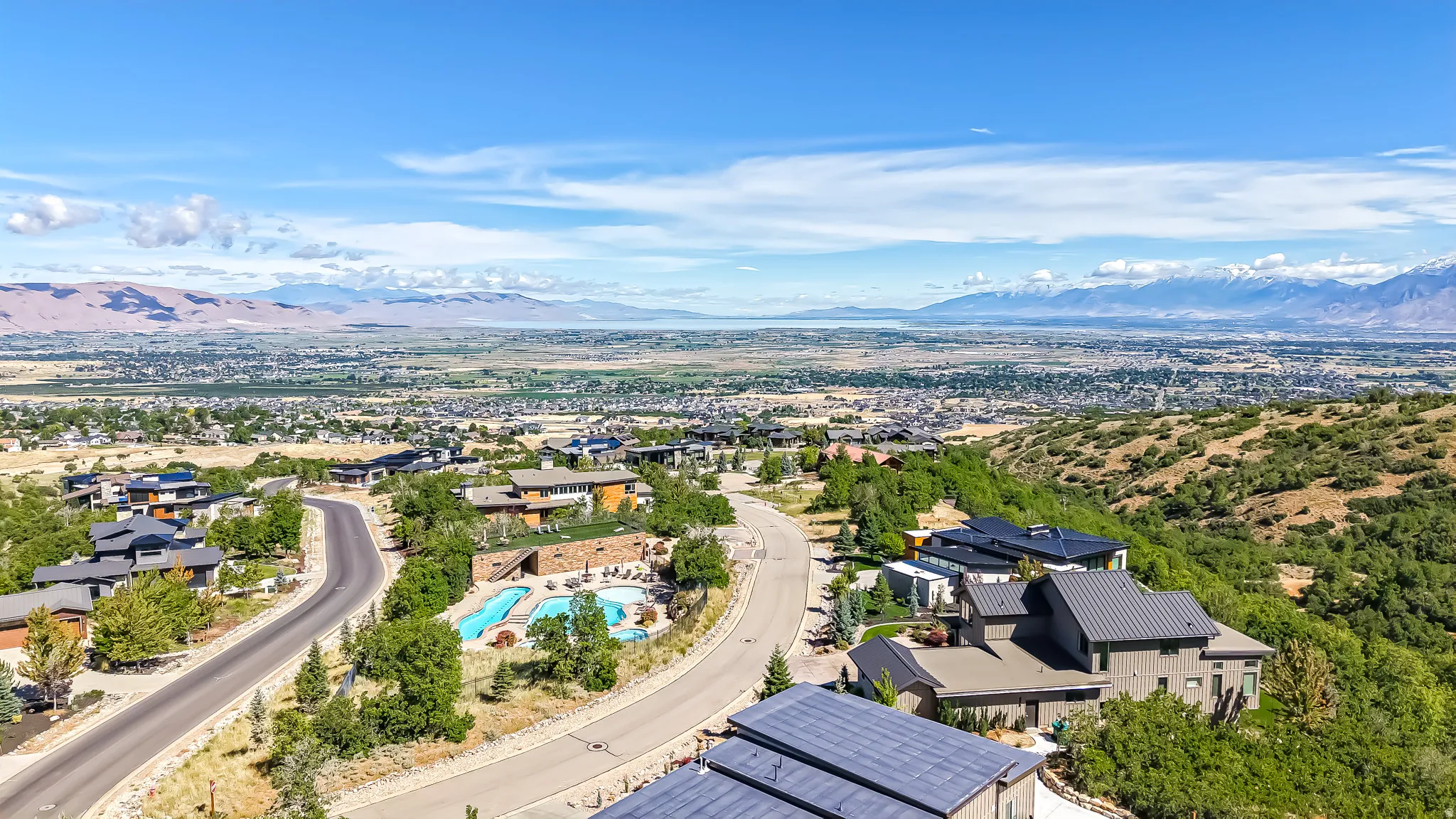 Hillside residential community featuring contemporary homes with dark-toned roofs and a community swimming pool area
