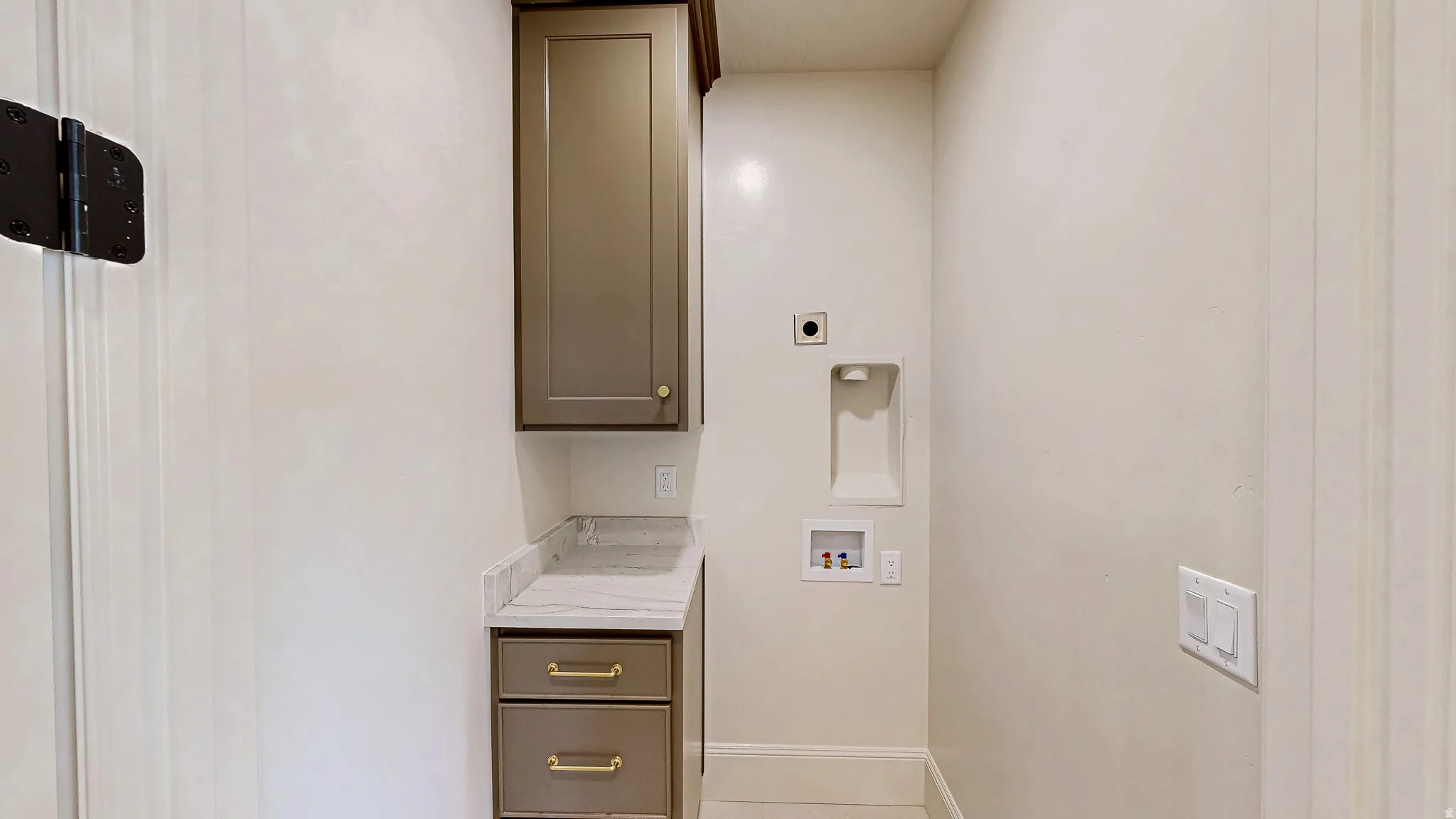 Utility room featuring built-in cabinetry with brass hardware, a light-toned countertop, and provision for laundry appliances