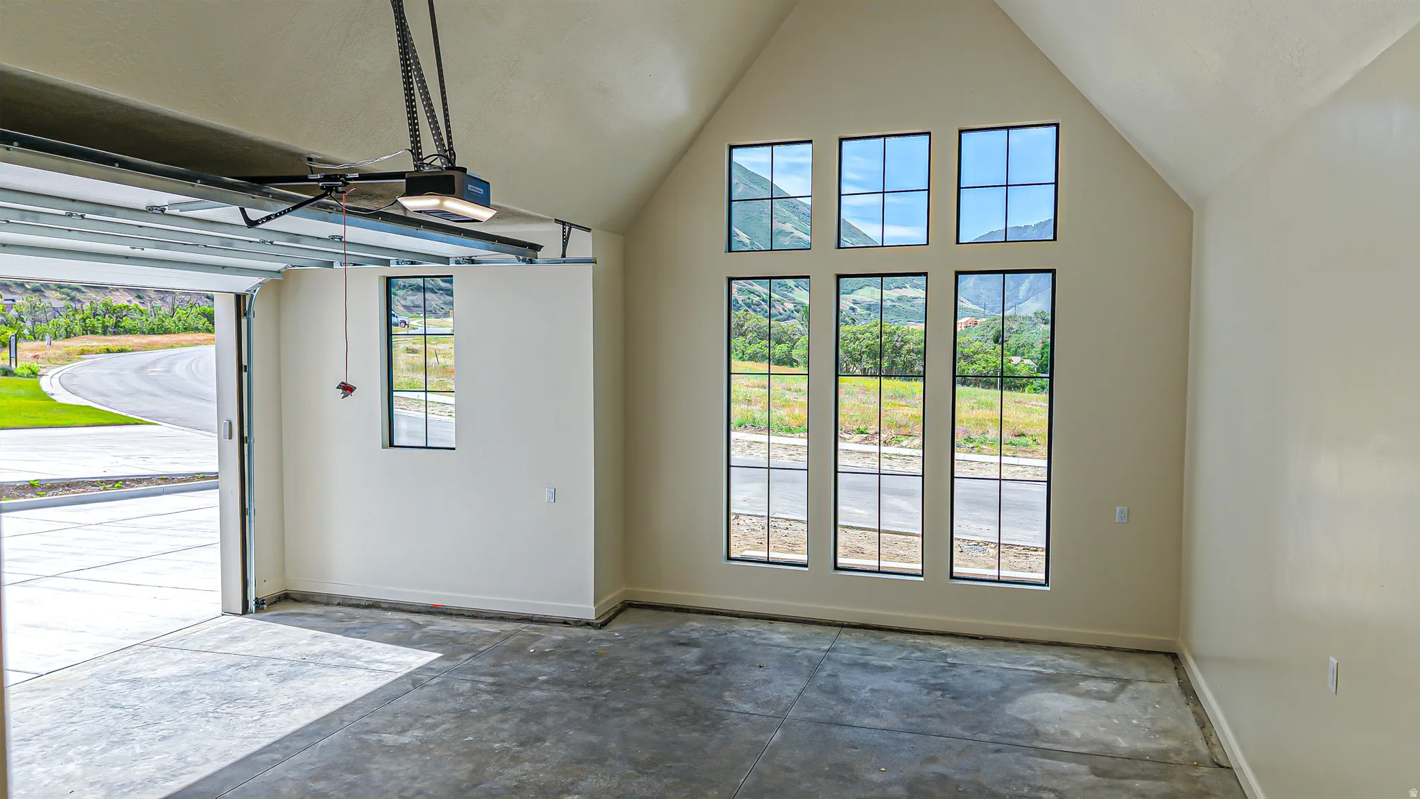 Vaulted garage space featuring a concrete floor, an automatic garage door opener, and a wall of six grid-pane windows