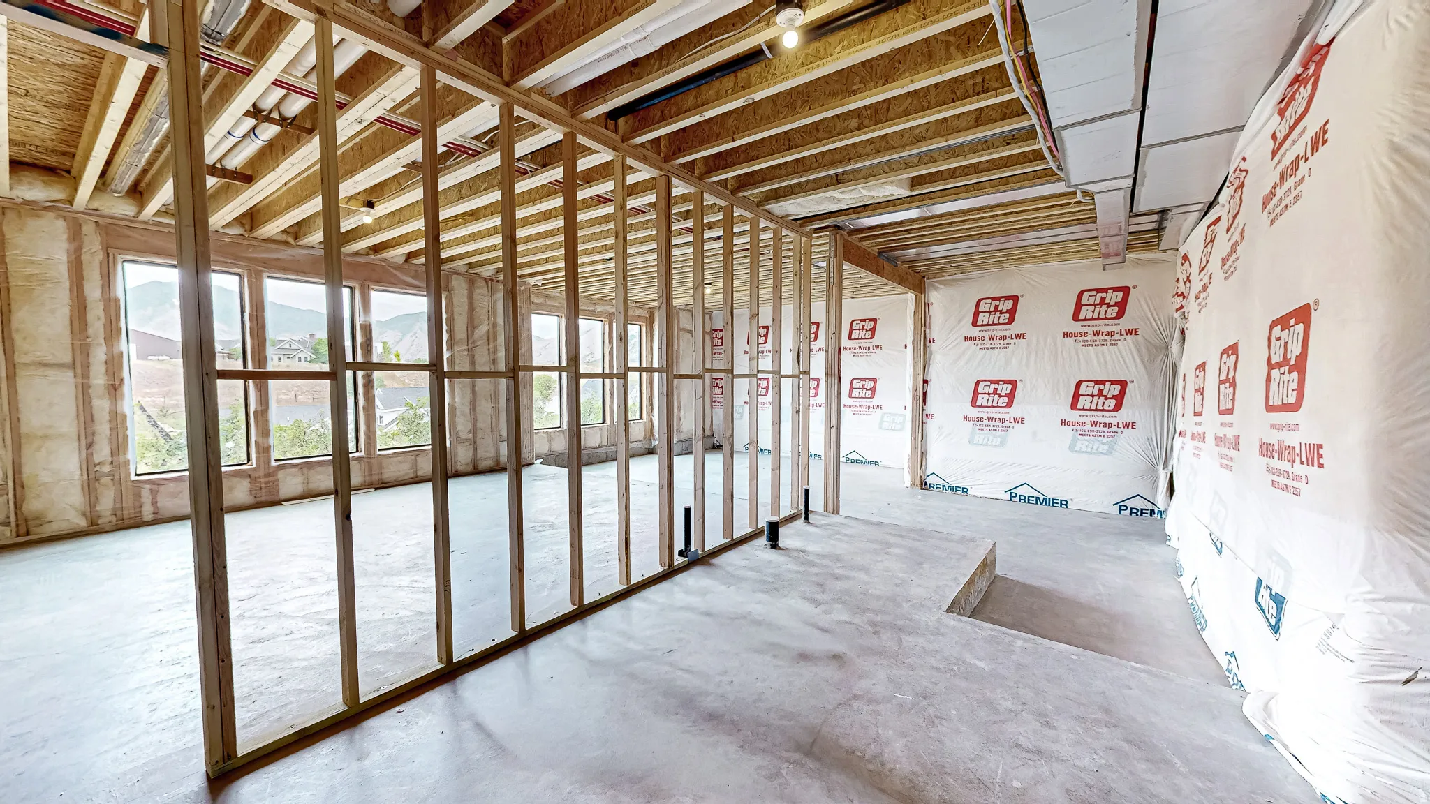 Spacious interior framing with multiple windows, exposed ceiling joists, concrete flooring, and partial wall sheathing