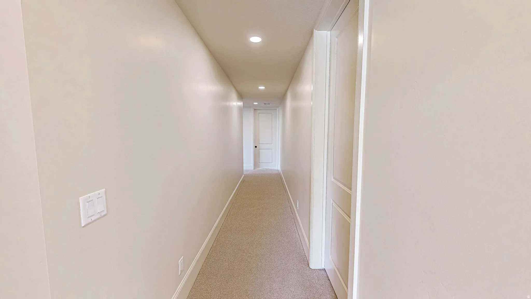Long hallway featuring recessed lighting, light-toned carpeting, and a white panel door with dark hardware