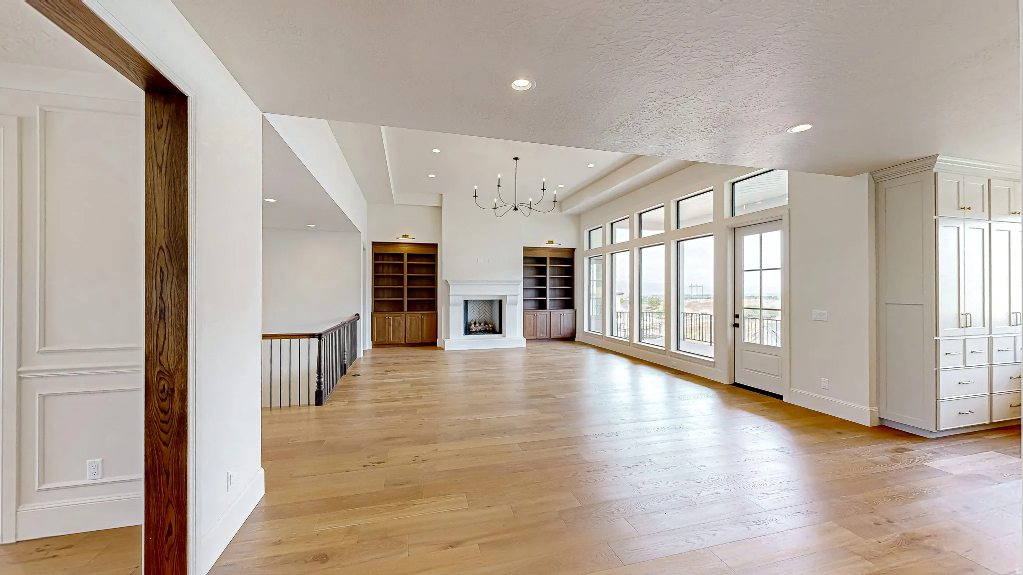 Spacious living area featuring light wood-finish flooring, a wall of large windows, a fireplace with a stone surround, built-in shelving, and a chandelier