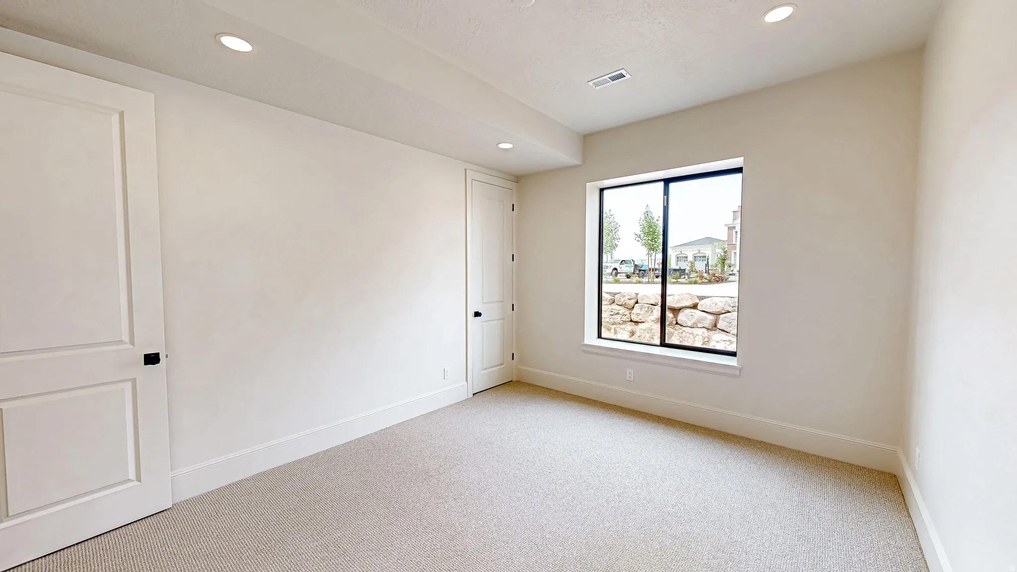 Carpeted interior space featuring recessed lighting, a large window, a rock retaining wall, and two paneled doors with black hardware