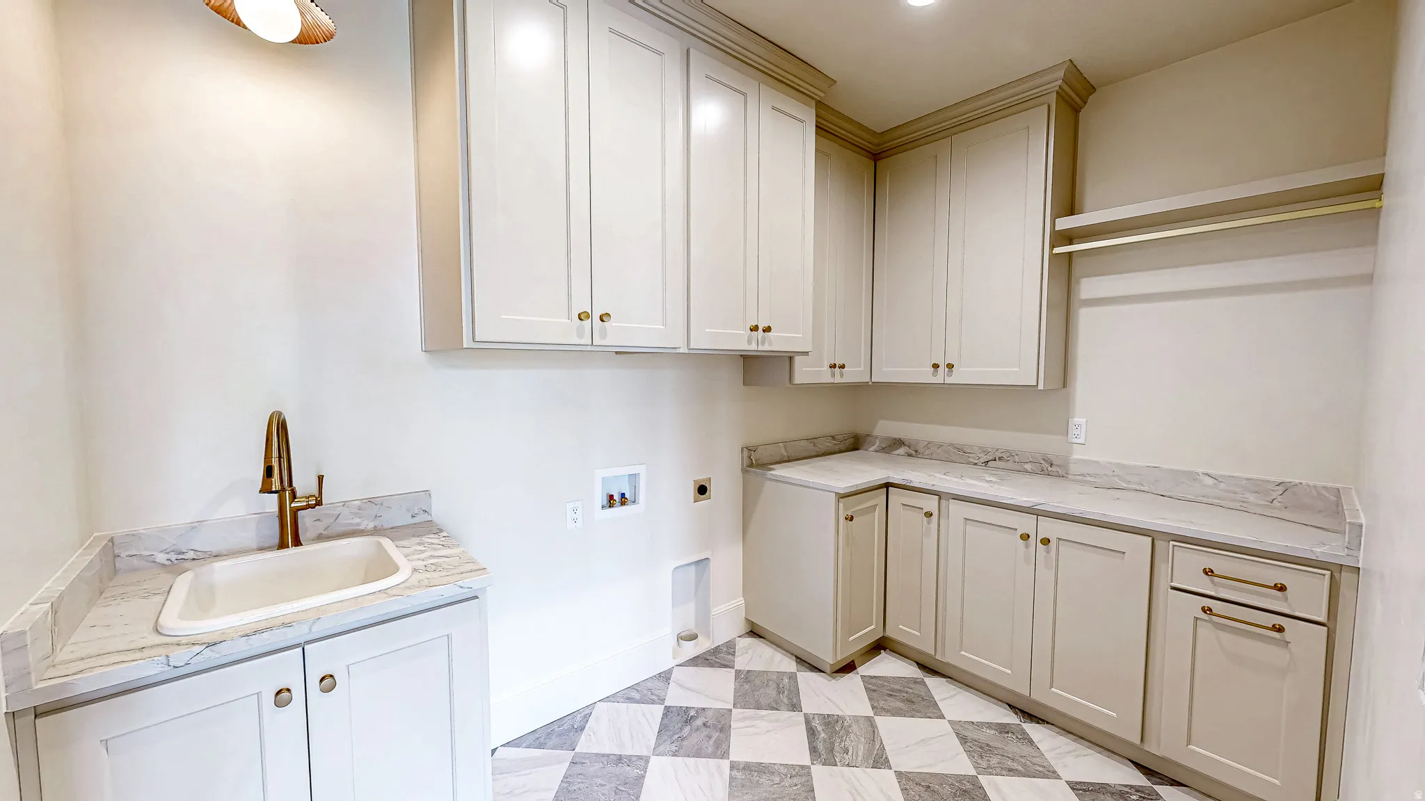 Laundry area featuring extensive cabinetry, checkerboard-patterned flooring, a utility sink with a brass-finish faucet, stone-finish countertops, and hanging rods