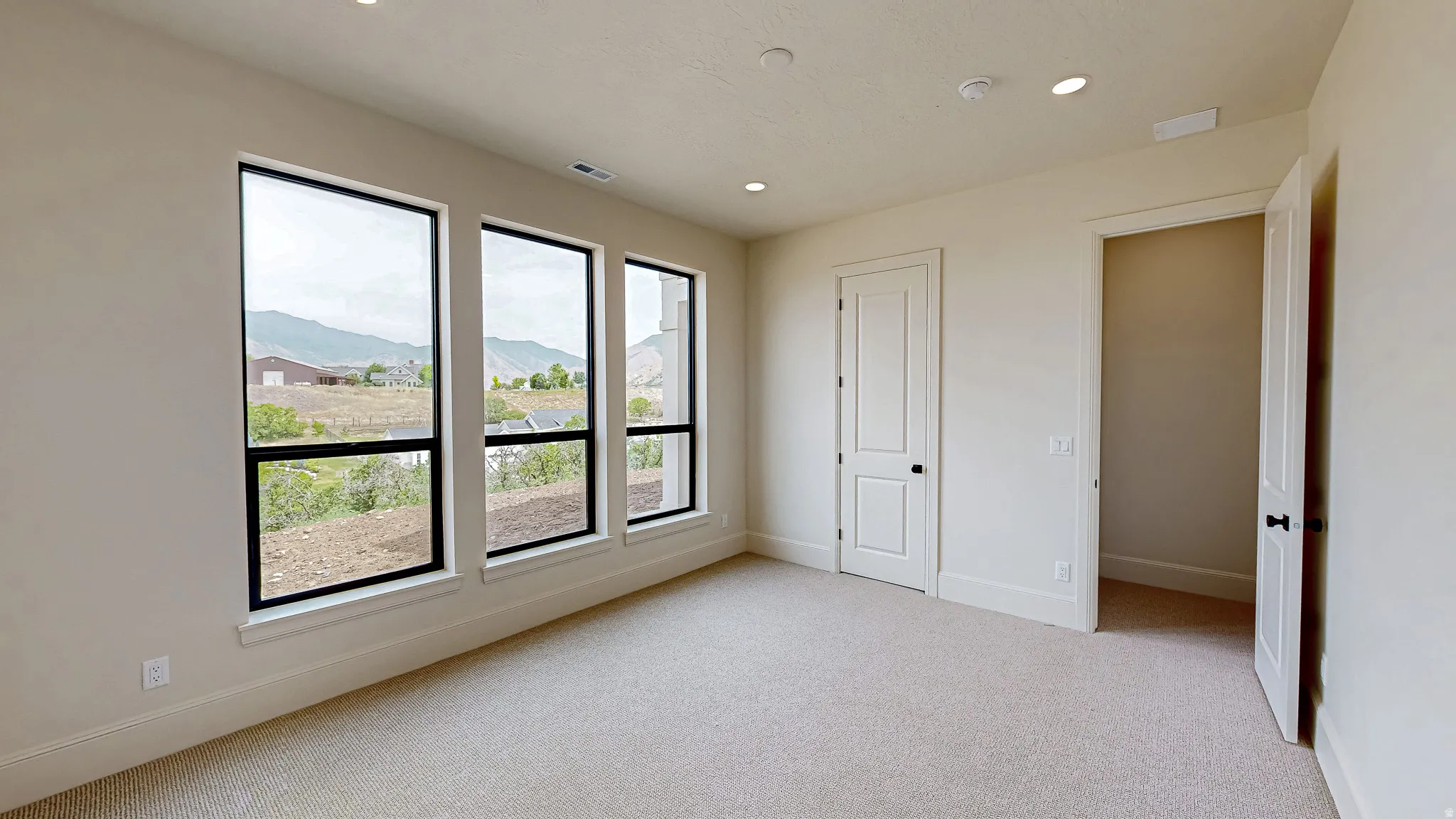 Room featuring three tall windows with black frames, offering expansive outdoor scenery