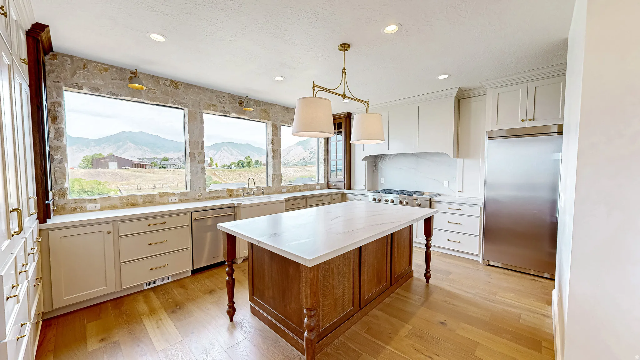 Gourmet kitchen with expansive mountain scenery, featuring a large center island with a stone-finish countertop, stainless steel appliances, abundant cabinetry, and wood-finish flooring