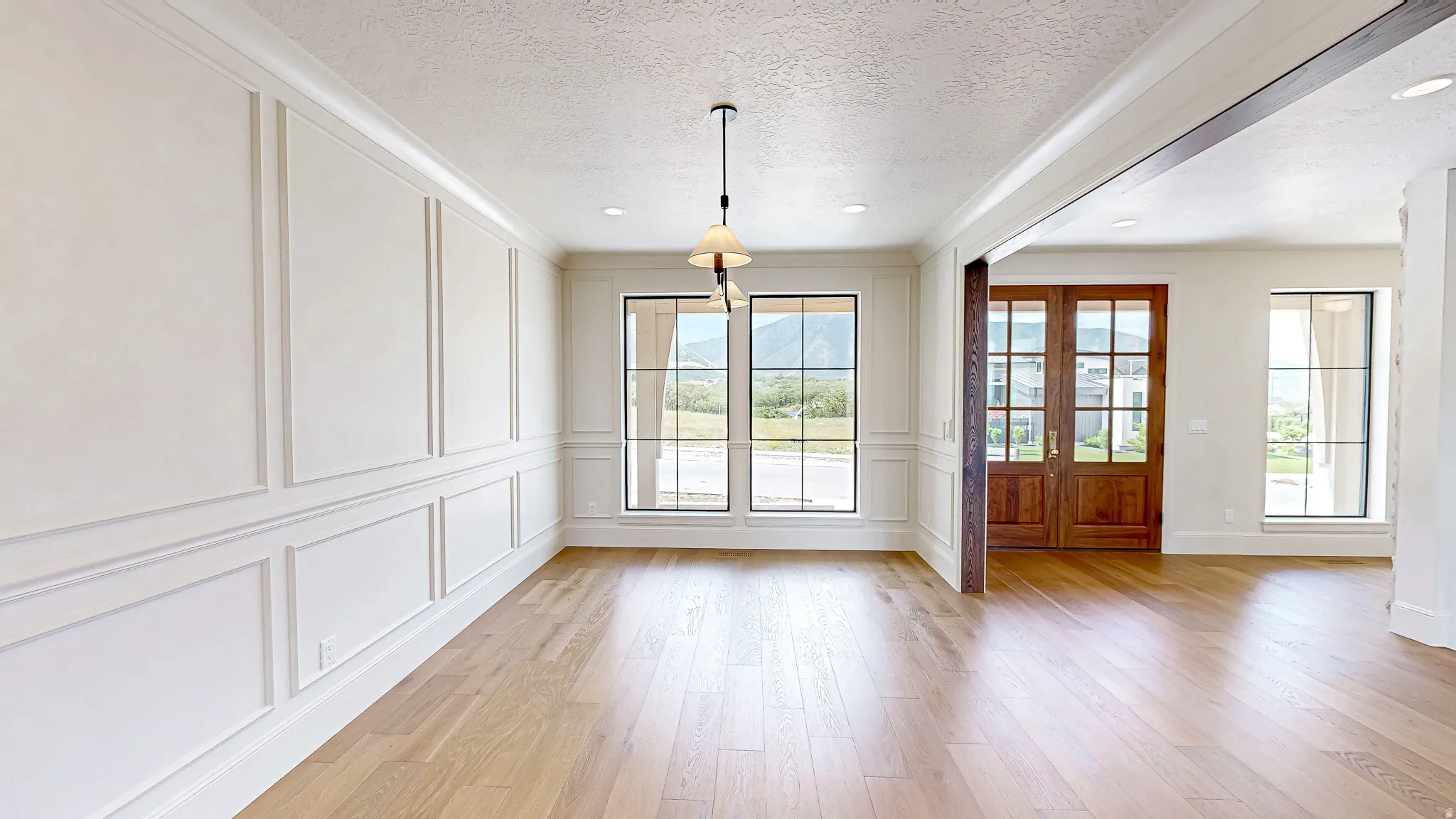 Spacious interior featuring light wood-finish flooring, white paneled wall detailing, and a multi-pane window with mountain scenery