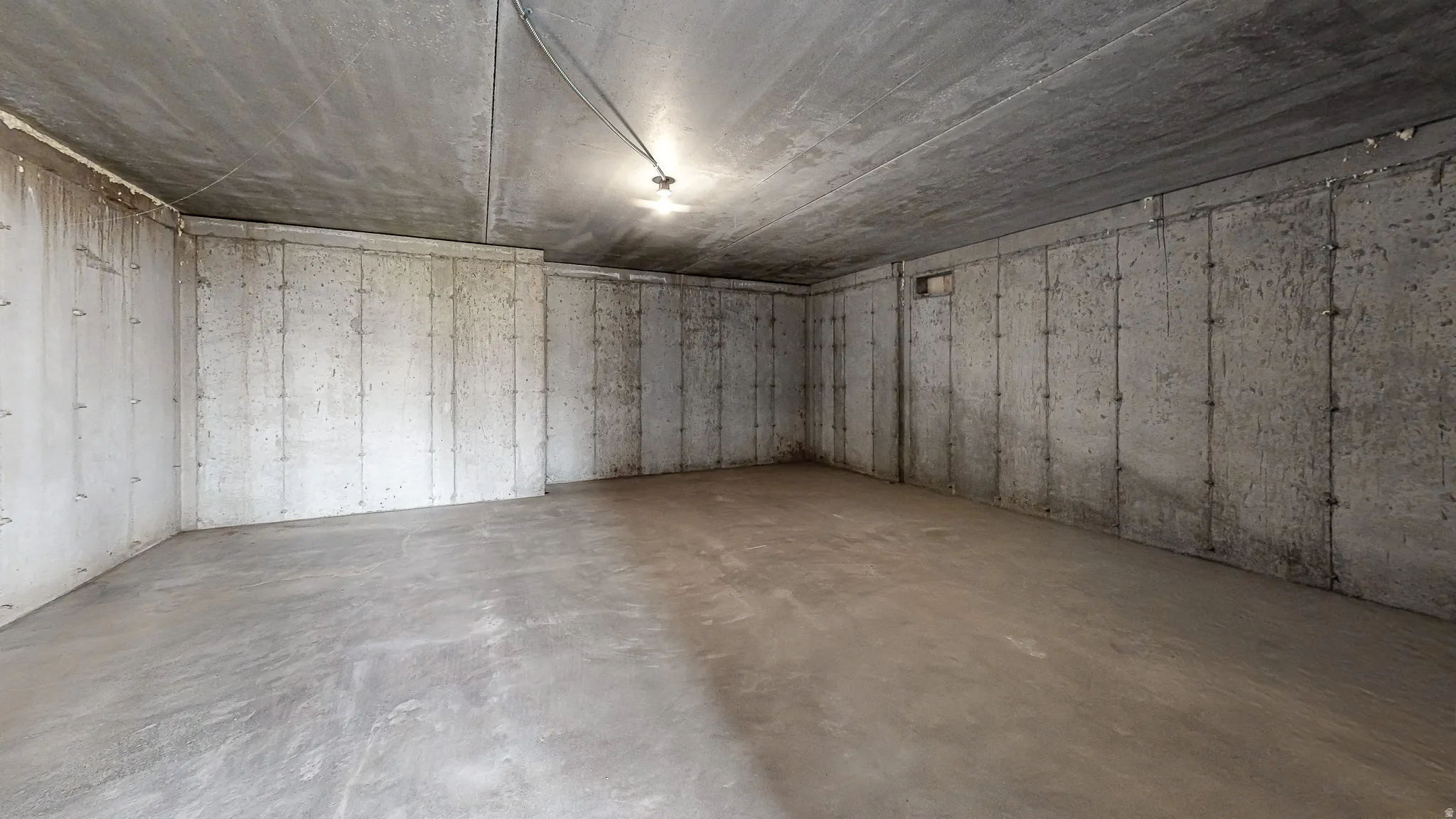 Unfinished concrete basement featuring exposed concrete walls, raw concrete floor, and overhead lighting