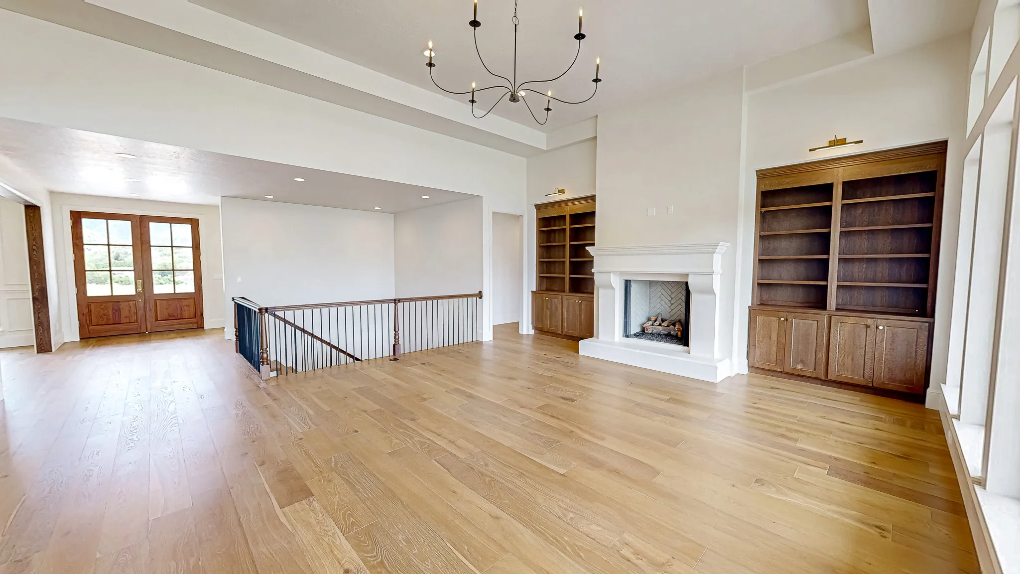 Expansive living area featuring light wood-finish flooring, a contemporary fireplace with a herringbone-patterned firebox, and built-in wood cabinetry with integrated shelving