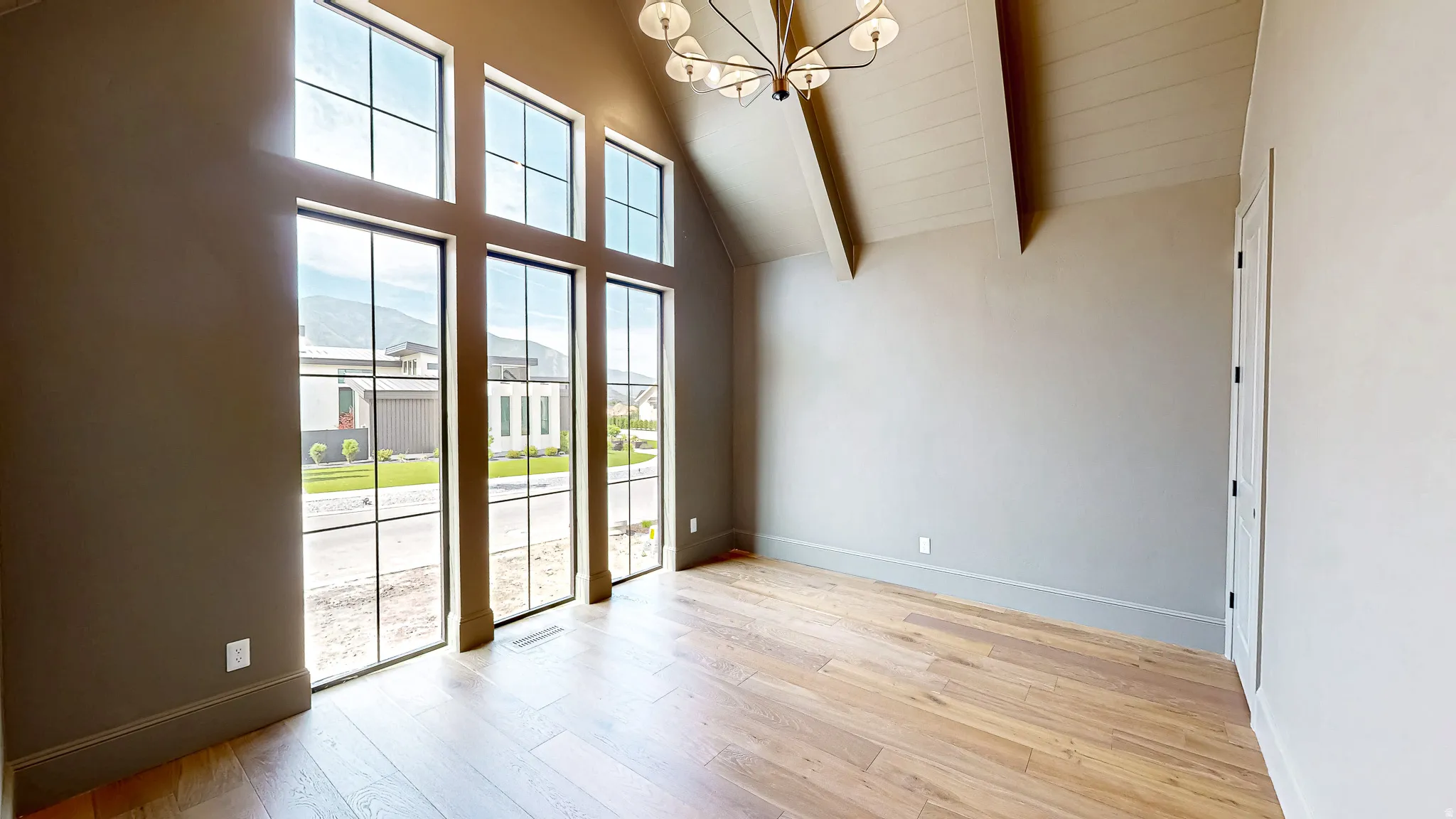 Room featuring floor-to-ceiling windows with black grids, wood-finish flooring, a vaulted ceiling with exposed beams, and a contemporary chandelier