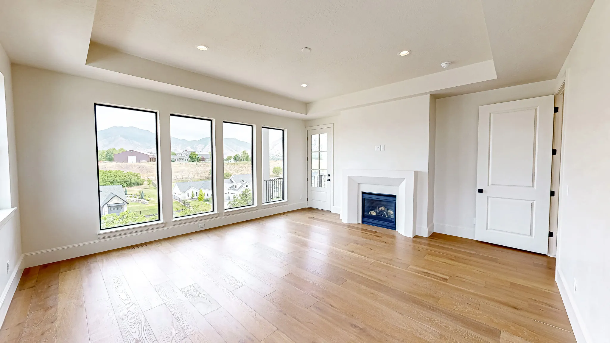Spacious room featuring wood-finish flooring, a contemporary fireplace, and a tray ceiling with recessed lighting