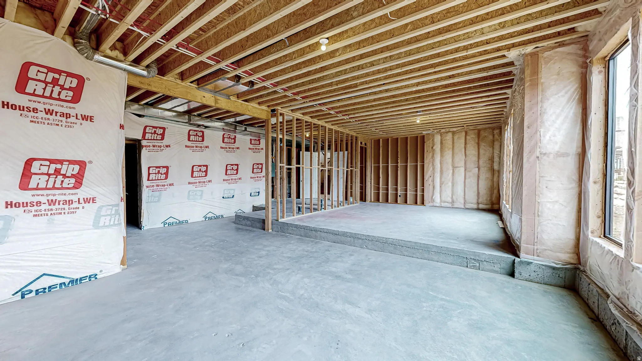 Unfinished basement featuring exposed wood framing, concrete flooring, and multiple windows allowing for natural illumination