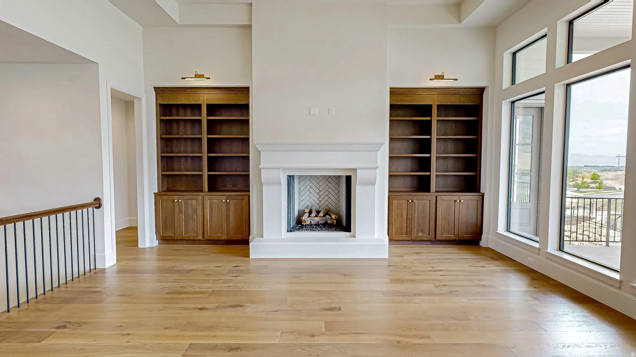 Spacious living area featuring a central fireplace with a herringbone pattern firebox, flanked by custom wood-finish built-in shelving units with integrated lighting