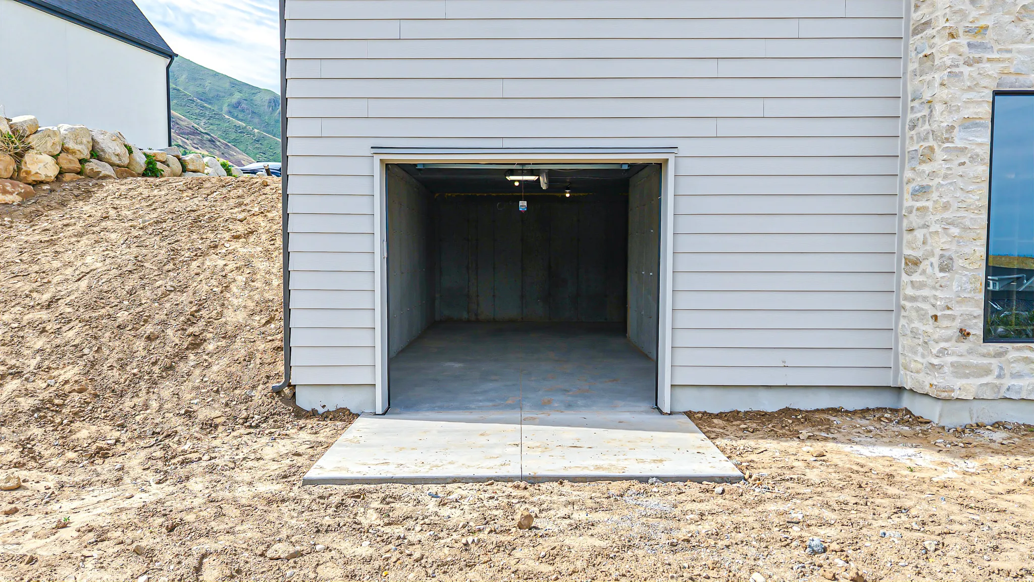 Garage entrance with concrete pad, light gray siding, and stone facade