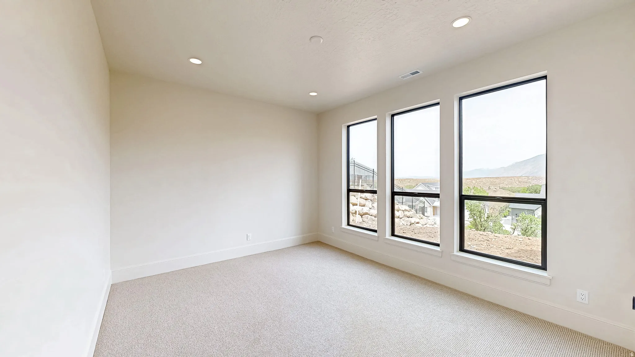 Room featuring three large vertical windows with black trim, recessed ceiling lighting, light-toned carpet, white baseboards, and neutral wall paint