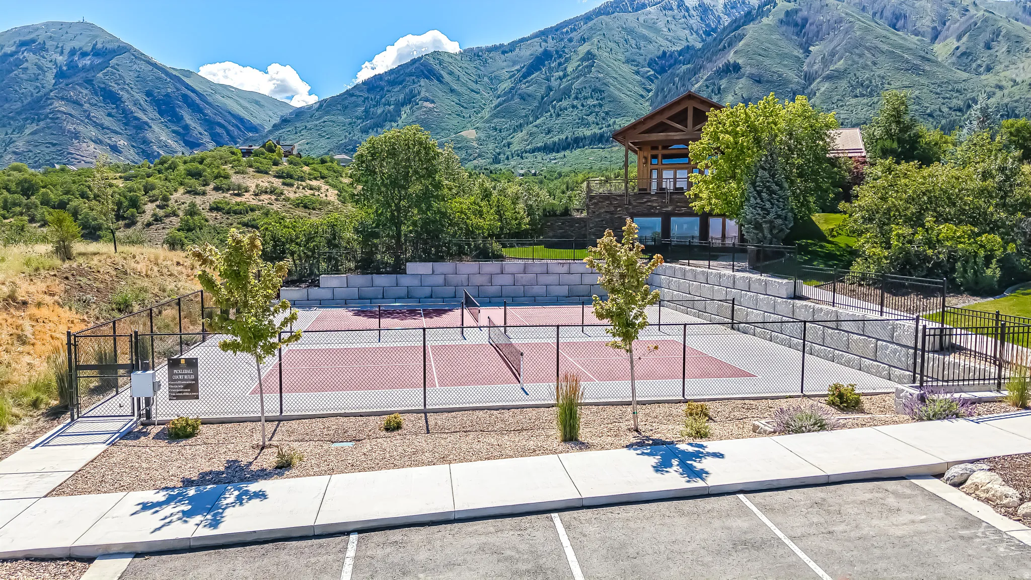 Fenced pickleball courts with two nets, surrounded by retaining walls and landscaping