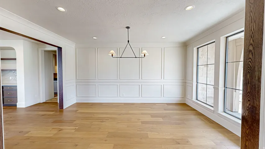 Spacious room featuring wood-finish flooring, wainscoting, recessed lighting, and a linear chandelier