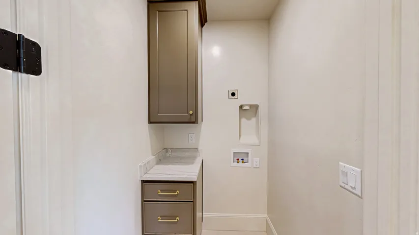 Utility room featuring built-in cabinetry with brass hardware, a light-toned countertop, and provision for laundry appliances