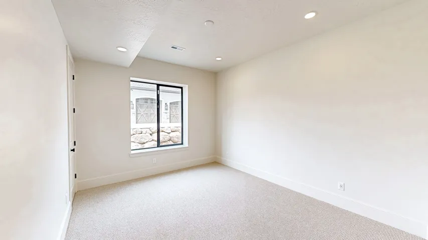 Recessed lighting illuminates this room featuring light-colored carpeting, white walls, and a window with black trim
