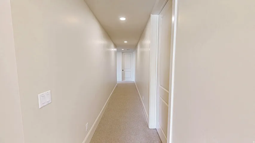 Long hallway featuring recessed lighting, light-toned carpeting, and a white panel door with dark hardware