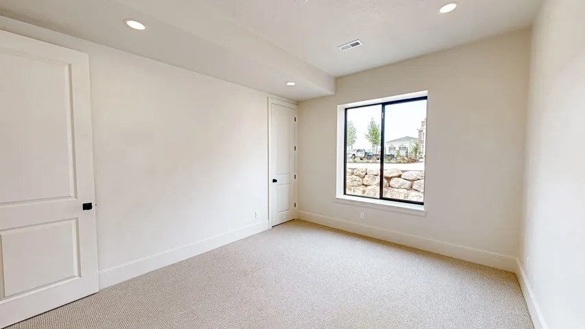 Carpeted interior space featuring recessed lighting, a large window, a rock retaining wall, and two paneled doors with black hardware