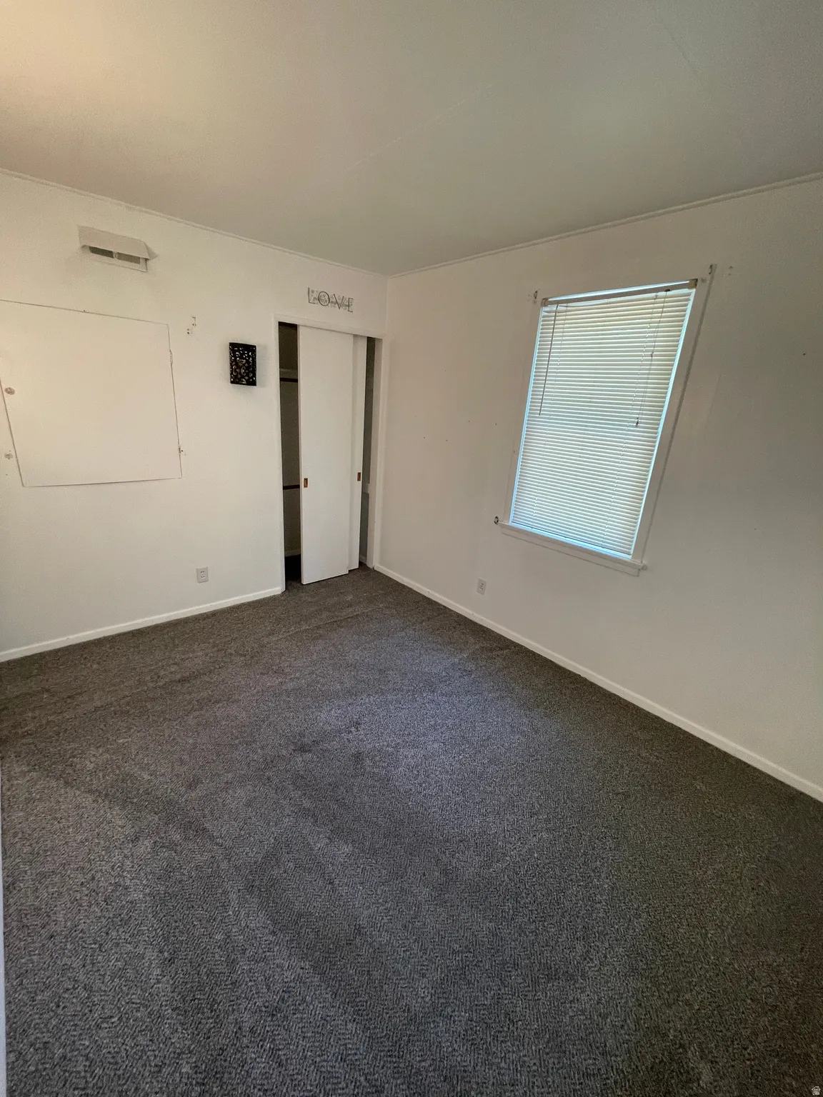 Room featuring dark gray carpet flooring, white walls, and a window with blinds