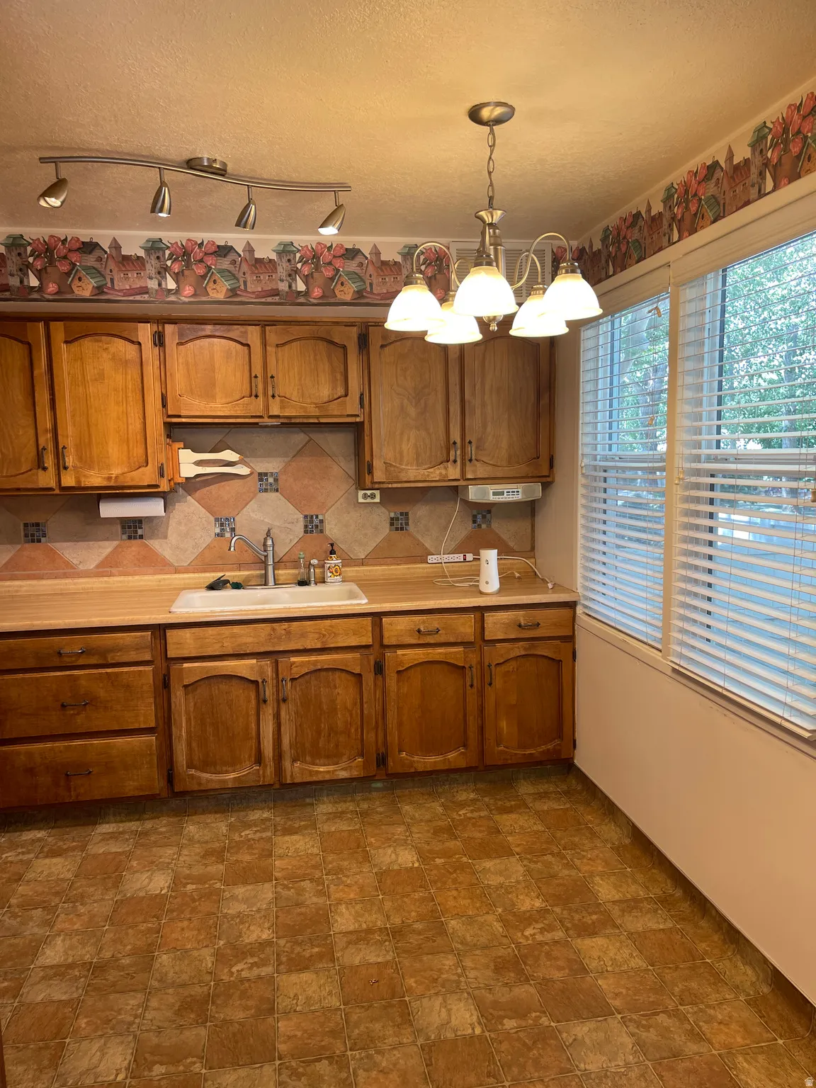 Kitchen area featuring wood cabinetry, laminate countertops, a tile backsplash, and checkerboard floor tiling